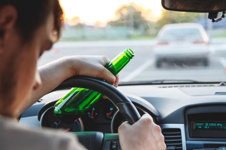 person driving behind steering wheel of car with bottle of alcohol
